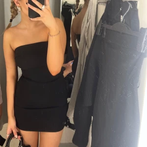 Svart axelbandslös kortklänning - Säljer en svart axelbandslös kortklänning med tight passform. Klänningen har en enkel och stilren design som sitter snyggt på kroppen. Helt oanvänd!