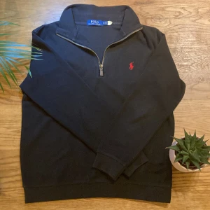 Svart half zip tröja från Polo Ralph Lauren - Säljer en snygg svart half zip tröja från Polo Ralph Lauren i storlek S. Passar ca 170cm lång. Den har en dragkedja vid halsen och det klassiska röda broderade logotypen på bröstet. 