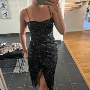 Svart prickig klänning med smala axelband - Säljer en svart klänning med vita prickar och smala axelband då den inte kommer till användning!