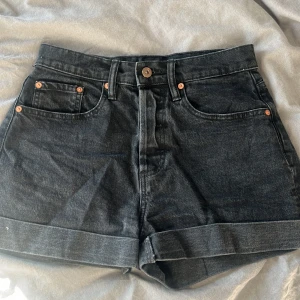 Svarta jeansshorts från 157 - Snygga svarta jeansshorts från 157 med klassisk femficksdesign och uppvikta benslut. Perfekta för varma dagar och enkla att matcha med allt. Stängs med fyra knappar, har bälteshällor och en cool, avslappnad vibe.