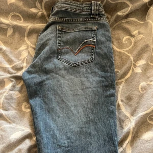Blåa low jeansboutcut från Teddy's Hyper - Klassiska blå jeansbyxor från Teddy's Hyper med fem fickor och snygga kontrastsömmar. Bakfickan har dekorativ broderad detalj i vitt och orange. Perfekta för en avslappnad stil.               Är från 2010 som nya!