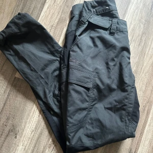 Friluftsbyxa Lundhags - Grå friluftsbyxor från Lundhags med flera fickor och robust design. Byxorna har bälteshällor, knapp och dragkedja i midjan samt praktiska sidofickor. Perfekta för dig som gillar funktionella och stilrena byxor. Använd en gång!