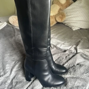Svarta höga stövlar med klack - Snygga svarta stövlar i skinn med hög klack och rund tå. Stövlarna går upp till knäet och har en stilren design som passar till många outfits. Perfekta för dig som vill ha ett par klassiska boots med lite extra höjd. Väldigt bekväma att gå i eftersom klacken är lite tjockare. 🌸Mycket bra skick!