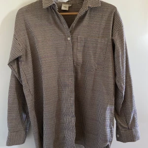 Brun och vit rutig skjorta från Ichi - Säljer en klassisk långärmad skjorta från Ichi i brunt och beige & svart rutigt mönster. Skjortan har en avslappnad passform, bröstficka och krage. Perfekt för en stilren och tidlös look. Så snygg! 