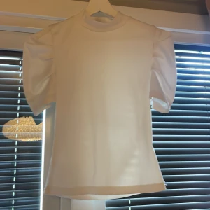 Vit topp med puffärmar från SHEIN - Säljer en vit topp från SHEIN med korta puffärmar och rund halsringning. Toppens material är slätt och har en stilren design som passar perfekt till olika outfits. Enkel men ändå trendig med fokus på ärmarnas volym.