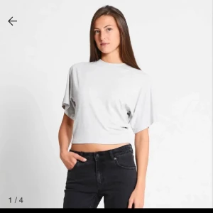 Ljusgrå croppad t-shirt - Säljer en enkel och stilren ljusgrå croppad t-shirt med korta ärmar och rund hals. Perfekt till jeans eller kjol för en avslappnad look.