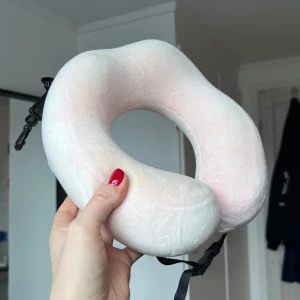 Ljusrosa mjuk nackkudde med spänne - En ljusrosa U-formad nackkudde i supermjuk plysch med justerbart svart spänne framtill. Perfekt för att ge stöd åt nacken under resor. Kudden har en diskret dragkedja på sidan och är lätt att ta med sig. Går även att ”rulla ihop” till en liten boll så den tar ännu mindre plats. Önskar du veta exakta mått? Tveka inte att höra av dig!