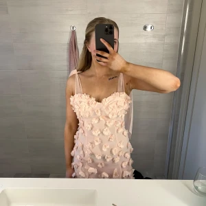 Rosa långklänning från ASOS - Säljer en fantastisk rosa långklänning från ASOS med 3D-blommor över hela klänningen. Den har en romantisk och elegant design, perfekt för speciella tillfällen. Klänningen har axelband och har en vacker passform som framhäver figuren. 🌸 kommer från asos kollektion LUXE 
