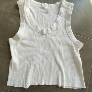 Vit ribbad croppad linnetopp från Brandy Melville, stl S - Säljer en vit ribbad croppad linnetopp från Brandy Melville. Toppen är ärmlös med rund halsringning och har en mjuk, stretchig bomullskvalitet. Perfekt till varma dagar eller som lager på lager-plagg.