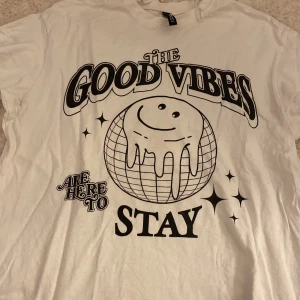 Vit t-shirt med tryck från H&M Divided - Vit t-shirt från H&M Divided med stort svart tryck på framsidan: 'The Good Vibes Are Here To Stay' och en smiley på en jordglob. Storleken är xxs men den ska vara väldigt oversized. Passar bra att sova i. Kontakta gärna innan köp🤗