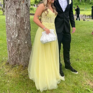Gul bal klänning - Säljer min så fina balklänning som endast är använd en gång. Klänningen är uppsydd för min längd och jag är 162 cm och hade på mig högklackat. Jag brukar bära S/M men bak i ryggen finns band som är justerbara så man kan dra åt klänningen som man vill. Köpt på Johans högtidskläder i Göteborg. Nypris 5000kr.