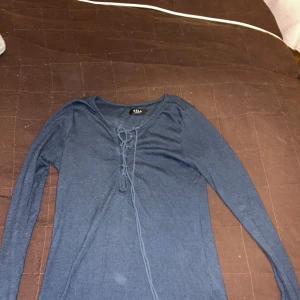 Mörkblå ribbad tröja från Vila - Säljer en mörkblå långärmad tröja från Vila med ribbad struktur och snörning framtill vid halsen. Perfekt för lager-på-lager och enkel att styla till olika outfits.