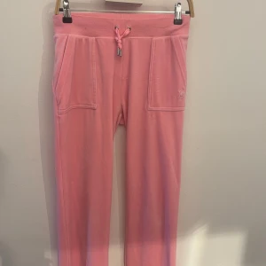 Rosa mjukisbyxor från Juicy Couture - Säljer ett par klassiska rosa mjukisbyxor från Juicy Couture. Byxorna har resår och snörning i midjan, två stora fickor fram och två fickor med knappar bak. Mjukt och skönt material som ger en avslappnad look.