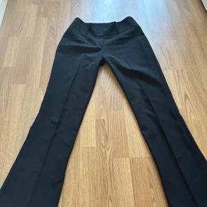 Svarta kostymbyxor med bootcut - Svarta kostymbyxor med bootcut-modell och hög midja. Byxorna har en klassisk och stilren look, perfekta för en dressad outfit. Tillverkade i ett mjukt och följsamt material som ger en snygg passform.