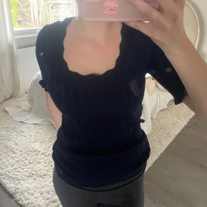 Mörkblå ribbad topp med fyrkantig ringning - Säljer en mörkblå stickad topp med korta puffärmar och snygg fyrkantig ringning. Perfekt för dig som vill ha en stilren men ändå trendig look. Använd max 2 ggr!