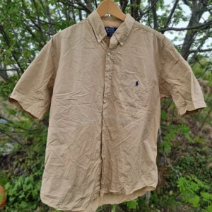 Beige kortärmad skjorta från Polo Ralph Lauren - Beige ralph lauren skjorta  Hej! Jag säljer en riktigt snygg kortärmad ralph lauren skjorta i storlek L. Skicket är 9/10 ⭐️ med inga fläckar eller defekter. Väldigt fin och perfekt plagg inför sommaren som är nära 🌞!   Orginalpris: 1500kr Mitt pris: 329kr Går med på bud så buda gärna! Skriv också om ni har några frågor.