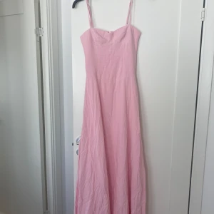 Ljusrosa långklänning från Peppermayo - Säljer en ljusrosa långklänning från Peppermayo med smala axelband och figurnära passform upptill. Klänningen har en enkel, elegant design och är tillverkad i ett lätt material som faller fint. Perfekt för sommarens tillfällen samt bal.