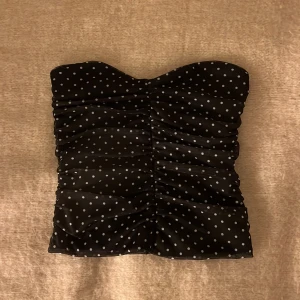 Svart prickig tubtopp från BikBok - Säljer en svart tubtopp från BikBok med vita prickar och rynkade detaljer framtill. Super söt!! 💕Toppen är axelbandslös och har en figurnära passform, perfekt för att skapa en trendig look. Säljer då den inte används ! 💕