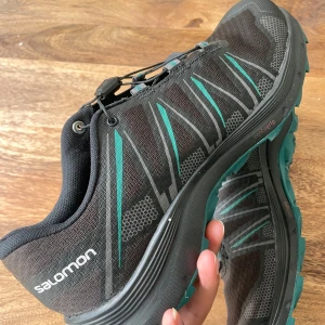 Svarta Salomon trailskor med turkosa detaljer - Säljer ett par svarta Salomon trailskor med turkosa detaljer och grov sula för bra grepp. Använda ett par gånger 