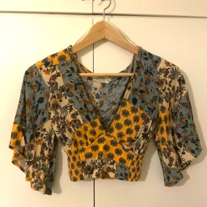 Croppad blus med volangärm - Superfin blommig croppad blus i blått, gult och vitt med v-ringning och volangärmar. Perfekt för vår och sommar, med omlottkänsla och lätt material. Snygg till både jeans och kjol! Köpt på Pull&Bear och aldrig använd!