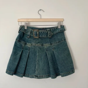 Jeanskjol med bälte och veck - Säljer en cool jeanskjol i blå denim med bredt bälte och stora veck. Kjolen har en kort passform och markerad midja med bälteshällor och spänne. 