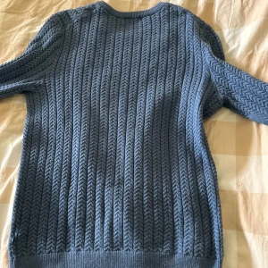 Blå stickad tröja från J.Lindeberg - Säljer en blå stickad tröja från J.Lindeberg med snyggt kabelstickat mönster. Tröjan har rund halsringning och långa ärmar, perfekt för kyligare dagar. Stilren och enkel att matcha med olika outfits. Köpt på nk för 1800