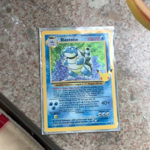 Blastoise Pokémonkort Base Set - Säljer ett klassiskt Blastoise-kort från Pokémon Base Set. Kortet har blå och gul ram, holografisk bild på Blastoise och 100 HP. Text och illustration är tydliga, och baksidan har den ikoniska Pokéball-designen.