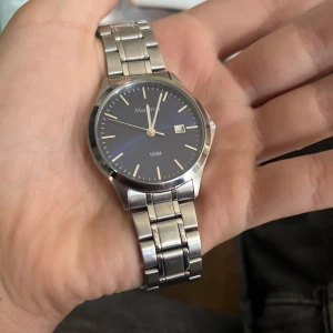 Silverfärgad klocka från Moretime med blå urtavla - Stilren klocka från Moretime med blå urtavla, silverfärgade visare och datumvisning. Armbandet är i metall och klockan är vattentät upp till 100 meter. Perfekt accessoar för dig som gillar klassisk design. Nytt batteri behövs.