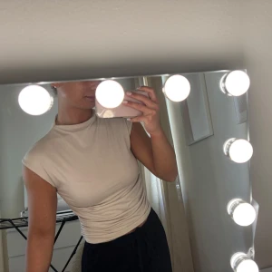 Beige ärmlös polotopp från Gina - Säljer en stilren beige ärmlös polotopp med tight passform. Perfekt att matcha med både jeans och kjol för en trendig look. Enkel och minimalistisk design utan synliga detaljer.