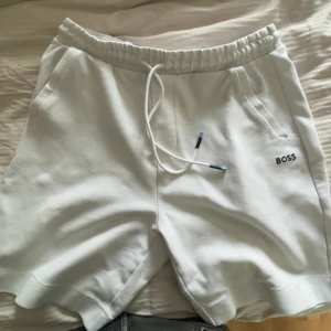 BOSS shorts  - Snygga vita shorts från BOSS med elastisk midja och snörning. Shortsen har två sidofickor och en diskret BOSS-logga broderad på vänster sida. Shortsen är använda ett par gången men är perfekt i skick, inga hål eller fläckar!! Storlek L men passar M perfekt BYTEN är tillgängligt!