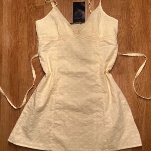 Ljusgul kort mini klänning från Brandy Melville - ljusgul klänning från Brandy Melville! v-ringad hals. Klänningen har små broderade blommor, spetsdetaljer vid halsen och knytband i midjan för en snygg passform ❤️HELT NY 