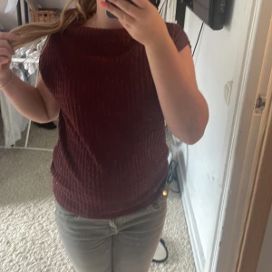 Vinröd topp med struktur - Vinröd topp med snygg struktur och rund halsringning. Modellen är ärmlös och har en något loose passform som gör den bekväm och enkel att styla. Perfekt för dig som gillar stilrena plagg med lite extra textur.