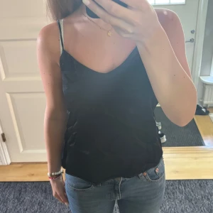 Svart linnetopp från Reserved XS - Säljer en svart linnetopp från Reserved i storlek XS. Toppen har tunna axelband och en lätt glansig finish som ger en snygg look. Perfekt till jeans eller kjol när du vill ha en enkel men stilren outfit.