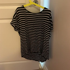 Svartvit randig topp från ONLY - Svartvit randig topp från ONLY Essentials med korta ärmar och rund hals. Toppen har en snygg dragkedja baktill som detalj och är gjord i mjukt, lätt material som känns skönt mot huden. Perfekt för dig som gillar en chill och stilren look.