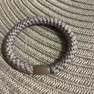 Grått flätat armband med pärldetalj - Snyggt och stilrent armband i grått med flätad design och en blank pärldetalj i mitten. Perfekt för dig som gillar enkel men cool accessoar. Passar till de flesta outfits och ger en modern touch.