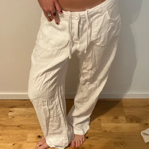 Vita linnebyxor med snörning - Snygga och luftiga vita linnebyxor med bred resår i midjan och snörning framtill. Byxorna har stora fickor fram och en avslappnad, loose passform. Perfekta för varma dagar och chill vibes.