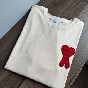 Beige t-shirt från Ami med rött hjärta - Snygg beige t-shirt från Ami med klassisk passform och korta ärmar | Skick: 9 / 10, knappt använd, utmärkt skick! | Vårt pris: 899 (inte hugget i sten) | Storlek: S | Tveka inte att höra av er med funderingar!