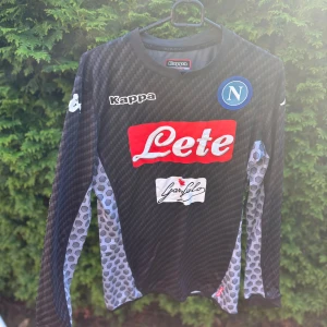 Napoli långärmad fotbollströja Milik - Napoli fotbollströja från Kappa i svart och grått med coolt vävt mönster och hexagon-detaljer på ärmarna. Långärmad modell med tryckta sponsorer, klubbmärke och Milik 99 på ryggen. Tillverkad i tekniskt, lätt material för bästa komfort på planen. Tröjan är perfekt för dig som samlar eller letar efter extremt sällsynta tröjor. Har ni några frågor är det bara att ni hör av er. Pris kan diskuteras👍