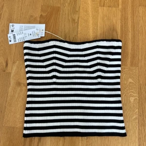 Randig bandeau tubtopp Gina Tricot - Snygg ribbad bandeau tubtopp från Gina Tricot i svart och vitt. Toppen har horisontella ränder och är stretchig för en tight passform. Perfekt att styla med jeans eller kjol för en cool look.