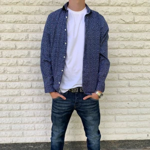 Blå mönstrad skjorta Jack & Jones, storlek S - Snygg blå skjorta från Jack & Jones med smått mönster i vitt och rött. Slim fit-modell med långa ärmar och knappar framtill. Perfekt för dig som vill ha en stilren men ändå unik look. Riktigt bra skick. Priset är inte hugget i sten!