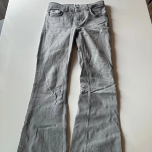 Grå bootcut jeans från 157, stl S - Snygga grå jeans från 157 i bootcut-modell med låg midja. Jeansen har klassisk femficksdesign och är tillverkade i bomullsmix med en mjuk känsla. Perfekta för dig som gillar en avslappnad men trendig look.