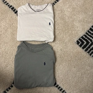 Två Polo Ralph Lauren t-shirts - Säljer två klassiska t-shirts från Polo Ralph Lauren. Ena är vit med mörkblå logga och diskret kontrastkant vid halsen, den andra är grå med samma mörkblå logga. Båda har rund hals och korta ärmar, tillverkade i mjuk bomull. Perfekt för chill och stilren look.