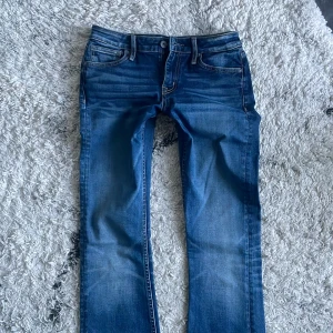 Crocker blå bootcut low waist jeans - Snygga Crocker jeans i klassisk blå tvätt med bootcut passform. Jeansen har fem fickor, tydliga kontrastsömmar och läderpatch bak i midjan. Tillverkade i slitstarkt denim med lätt slitning framtill för en cool look.