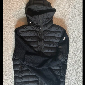 Moncler cardigan med huva - Säljer en svart moncler cardigan. Jackan är 100% autentisk då den är köpt på nk i Göteborg. Vissa subtila tecken på användning finns, ryggen är något noppig, och lite trådar syns vid huvan. Noppigheten går lätt att få bort med en noppmaskin. Hör av dig vid funderingar!
