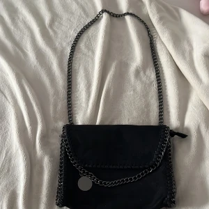 Svart axelväska med kedja - Snygg svart axelväska med grov kedja som axelrem och dekor runt kanterna. Väskan har ett lock och ett coolt innerfoder med leopardmönster samt dragkedja på insidan. Perfekt för dig som gillar edgy detaljer och stilren design. Finns ingen prislapp.