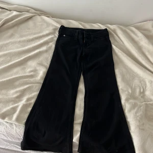 Svarta bootcut flare jeans Cheap Monday - Svarta flare jeans från Cheap Monday med låg midja och bootcut-ben. Jag har sytt dom kortare så dom passar nån som är runt 140/145 cm. Snygg passform med utsvängda ben och klassisk femficksdesign. Materialet är en mix av bomull, polyester och elastan för lite stretch. Perfekta för dig som gillar retrovibbar och statement-jeans.
