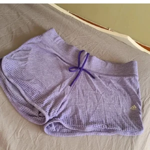 Lila träningsshorts från Adidas S - Snygga lila träningsshorts från Adidas med Climacool Aeroknit-teknologi. Shortsen har snörning i midjan och Adidas-logga på benet. Superlätta och luftiga. 