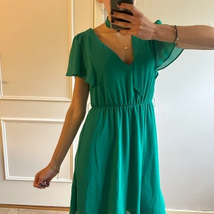 Grön kortklänning från Vila - Supersöt grön kortklänning från Vila med volangiga korta ärmar och knytband i midjan. Endast använd en gång 