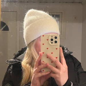 Vit ribbad stickad mössa - Säljer en vit, ribbad stickad mössa med bred uppvikt kant. Mössan har en klassisk, enkel form och är tillverkad i ett mjukt och fluffigt material som känns skönt mot huden. Perfekt för kalla dagar och ger en clean look till din outfit.