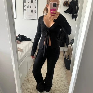 Svart långärmad knytblus Gina Tricot - Svart långärmad blus från Gina Tricot med djup v-ringning och knyt framtill. Toppen är croppad och har en slim passform som framhäver midjan. Perfekt att styla med höga jeans eller kjol för en trendig look.